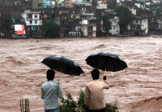 men with umbrellas watch muddy river