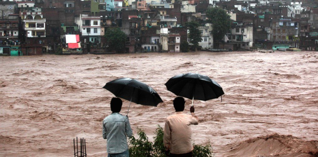 men with umbrellas watch muddy river