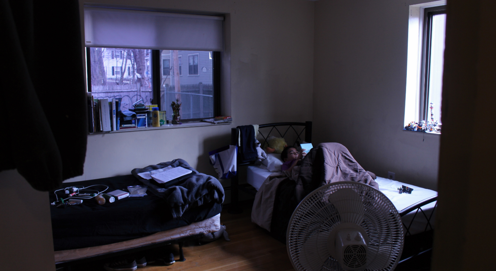 While sick with a fever, Martinez's 9-year-old son played video games from bed in their Jamaica Plain shelter. Martinez usually sleeps in the adjacent bed while her teenage daughter sleeps in a separate room. (Photo by Kelly Kasulis/GroundTruth)