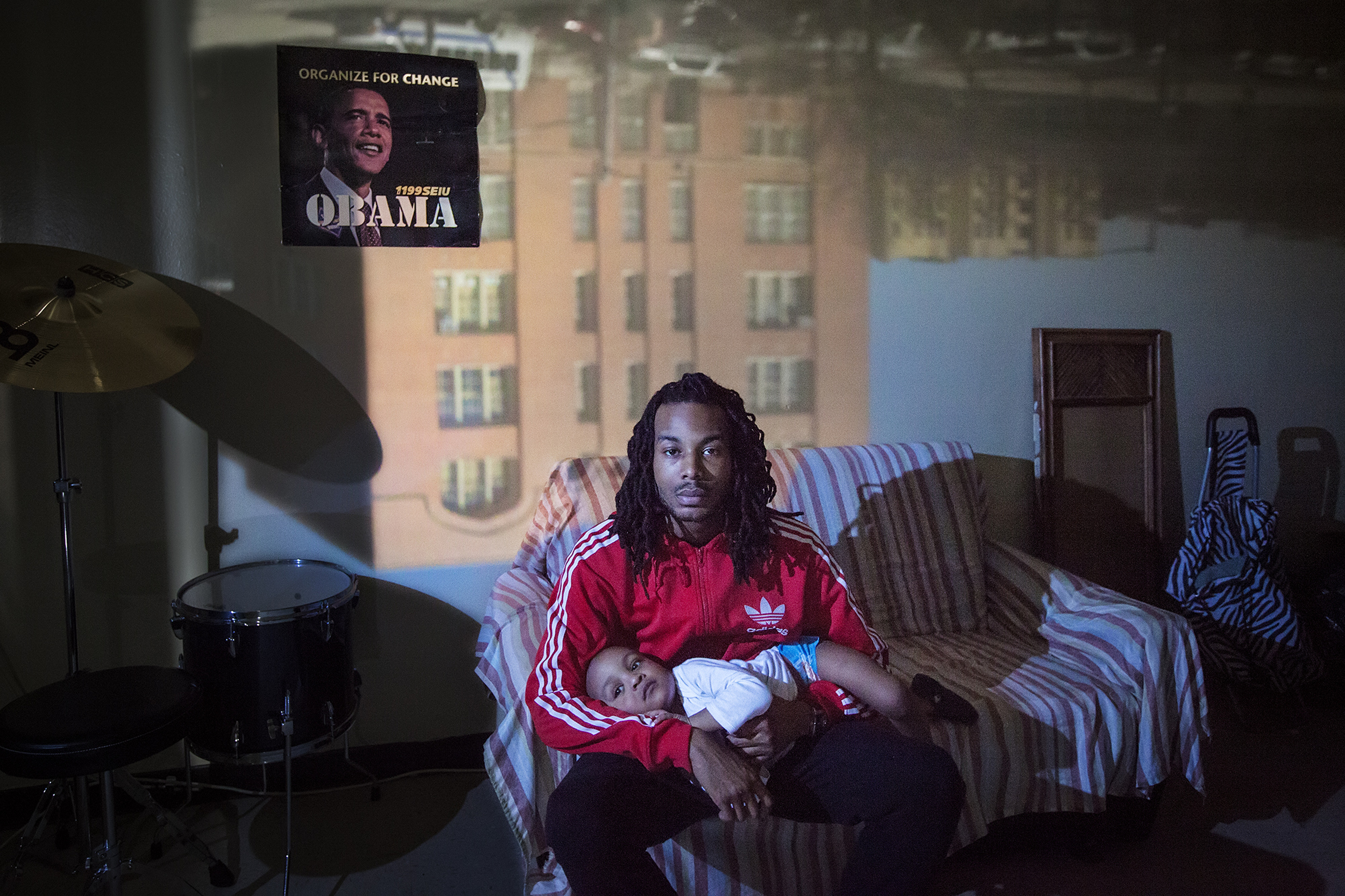 David "Prince" Pierce, 22, poses for a portrait with his son, Prince David Pierce, in East New York, NY on March 29, 2015. "I think about this all the time: who am I doin' this for? Can I really make this work with his mother or am I just running away from it 'cause I still want to live my life? I don't want to be tied down. I know a lot of cats that didn't see 21, didn't see 25, didn't see 30." Raising East New York (RENY) is a portraiture project about Black fathers where the photographer, Phyllis B. Dooney, uses a photographic technique called Camera Obscura to project the outside streets of East New York into the subjects apartment in real time.