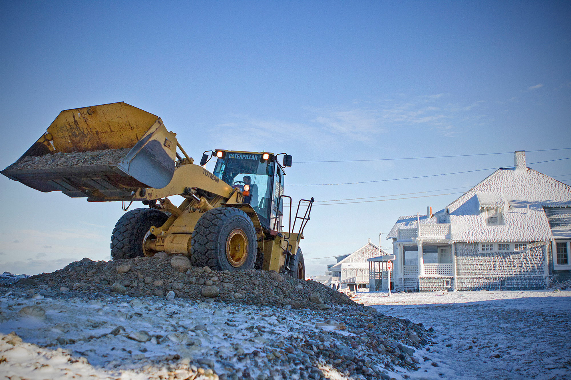 A wheel loader scoops up detritus from the ocean while rebuilding a road in Scituate following a 2015 winter storm that flooded dozens of homes, destroyed streets and power lines and even pulled buildings into the sea. Some homes in the town have been damaged and rebuilt more than 10 times with funding from the federal government and community tax money. (Photo by Lauren Owens Lambert/GroundTruth)