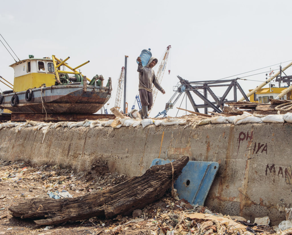 A worker in the Pluit district of North Jakarta carries a gallon of drinking water atop the seawall that flanks the area from the sea. Jakarta is sinking as a result of massive groundwater extraction. (Photo by Muhammad Fadli)