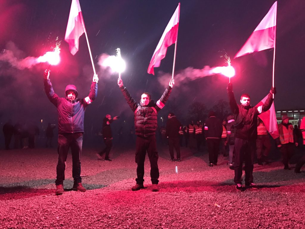 Young Poles stand silently while holding red flares and Polish flags and listen to speeches outside the National Stadium in Warsaw (Photo by Karolina Chorvath/GroundTruth)