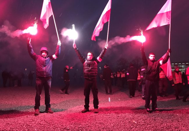 Young Poles stand silently while holding red flares and Polish flags and listen to speeches outside the National Stadium in Warsaw (Photo by Karolina Chorvath/GroundTruth)