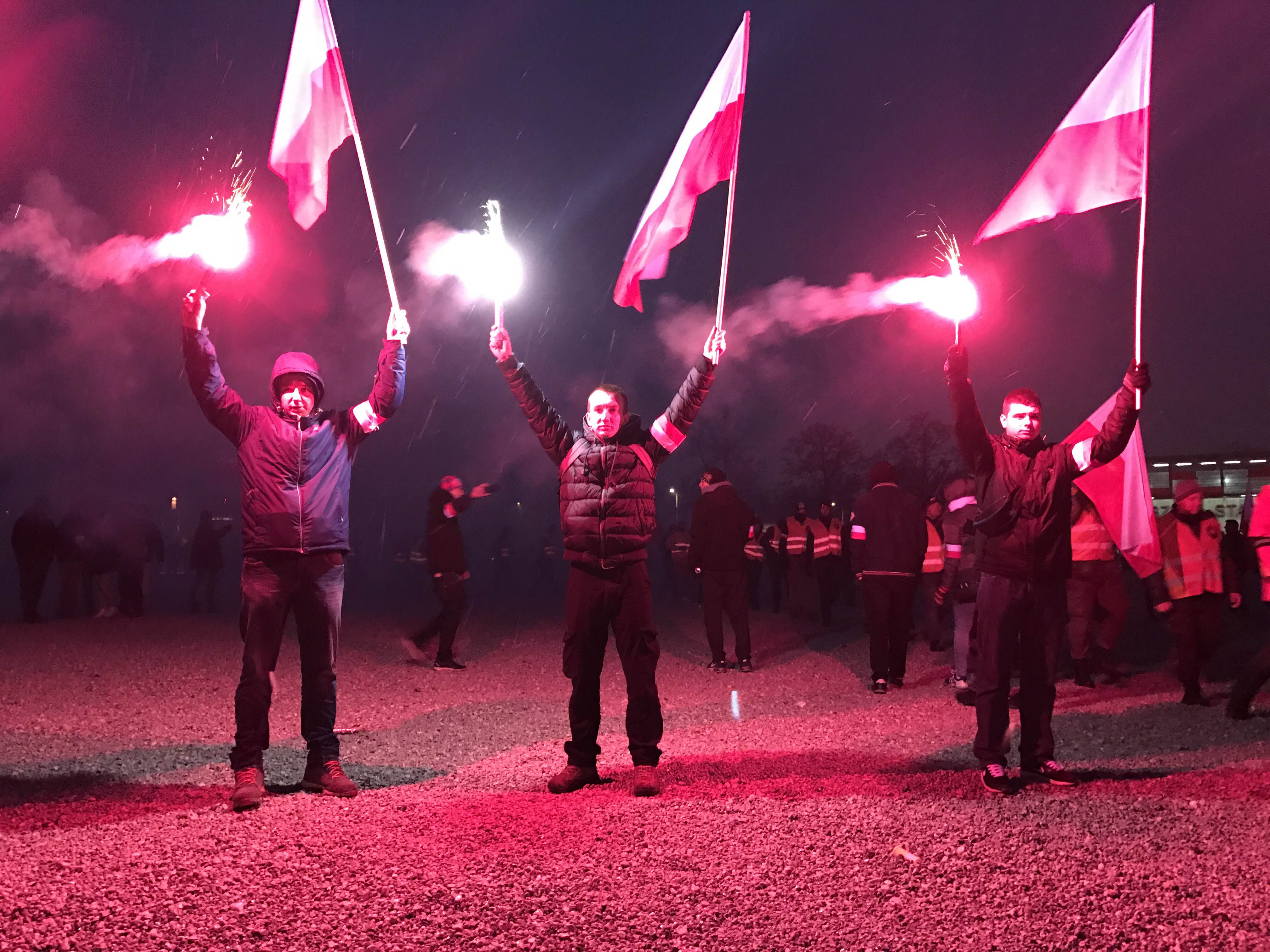 Young Poles stand silently while holding red flares and Polish flags and listen to speeches outside the National Stadium in Warsaw (Photo by Karolina Chorvath/GroundTruth)