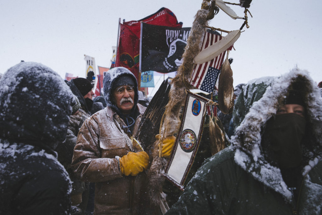 Glenn Scott, 60, a member of the Chippewa tribe and a Vietnam veteran, participates in a march of over 2,000 veterans from the Oceti Sakowin Camp to the police road block on Backwater Bridge on Monday, Dec. 5, 2016. Thousands of veterans deployed to Standing Rock to support the protest movement, offering to act as a human shield against police force. (Photo by Angus Mordant/GroundTruth)
