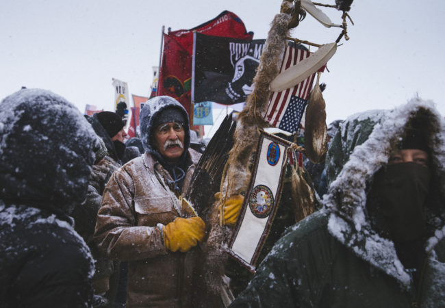 Glenn Scott, 60, a member of the Chippewa tribe and a Vietnam veteran, participates in a march of over 2,000 veterans from the Oceti Sakowin Camp to the police road block on Backwater Bridge on Monday, Dec. 5, 2016. Thousands of veterans deployed to Standing Rock to support the protest movement, offering to act as a human shield against police force. (Photo by Angus Mordant/GroundTruth)