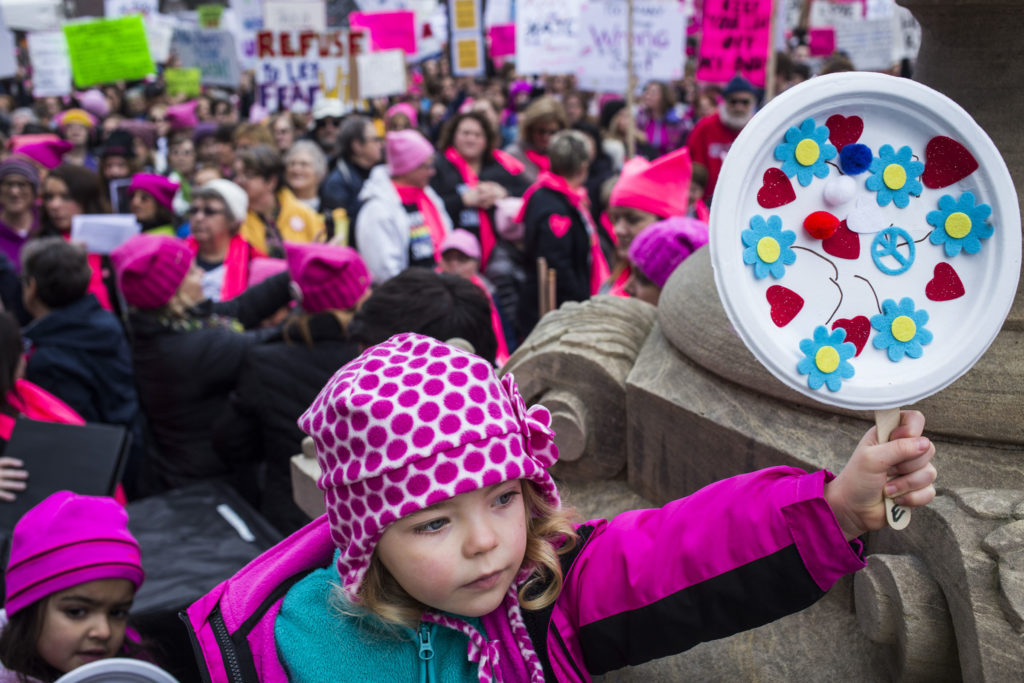 Amid a crowd of thousands, Emma Ilg, 4, of Novi, Mich., holds a sign as she's propped up on a railing for the Women's March on Lansing outside of the Michigan State Capitol Building in Lansing, Mich., on Saturday, January 21, 2017. (Photo by Brittany Greeson/GroundTruth)