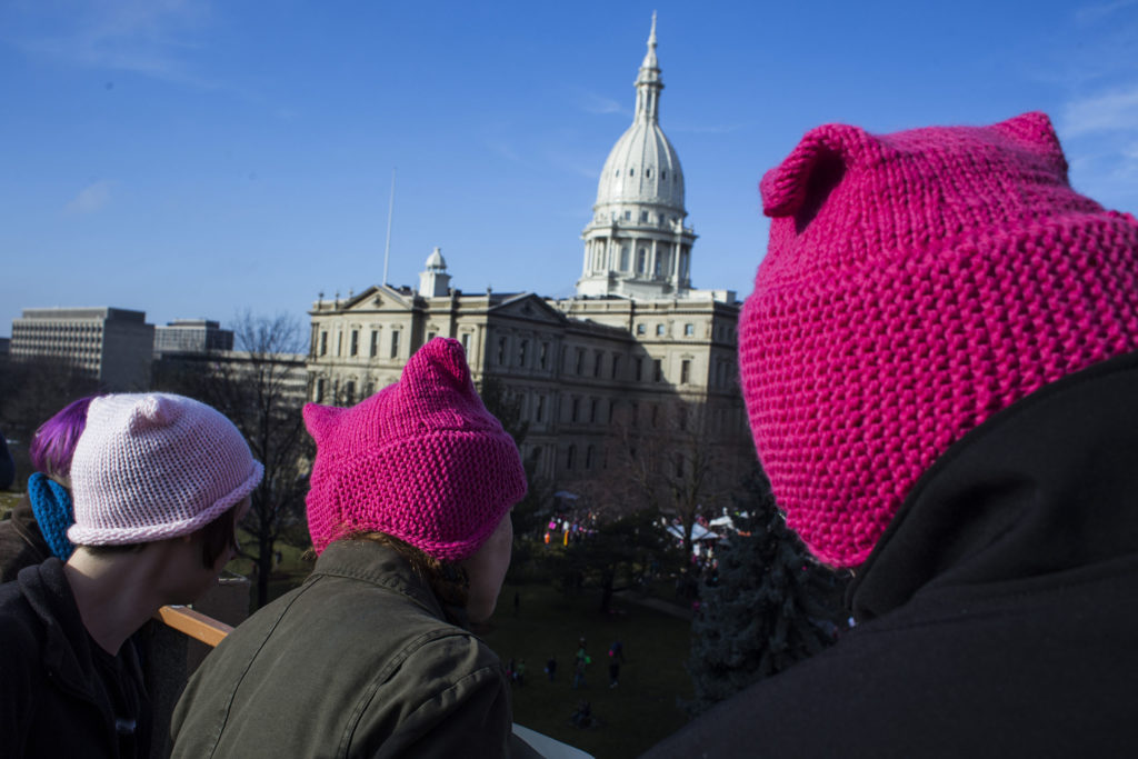 People wearing pink hats gaze at attendees from a nearby parking garage during the Women's March outside of the Michigan State Capitol Building in Lansing, Mich., on Saturday, January 21, 2017. (Photo by Brittany Greeson/GroundTruth)
