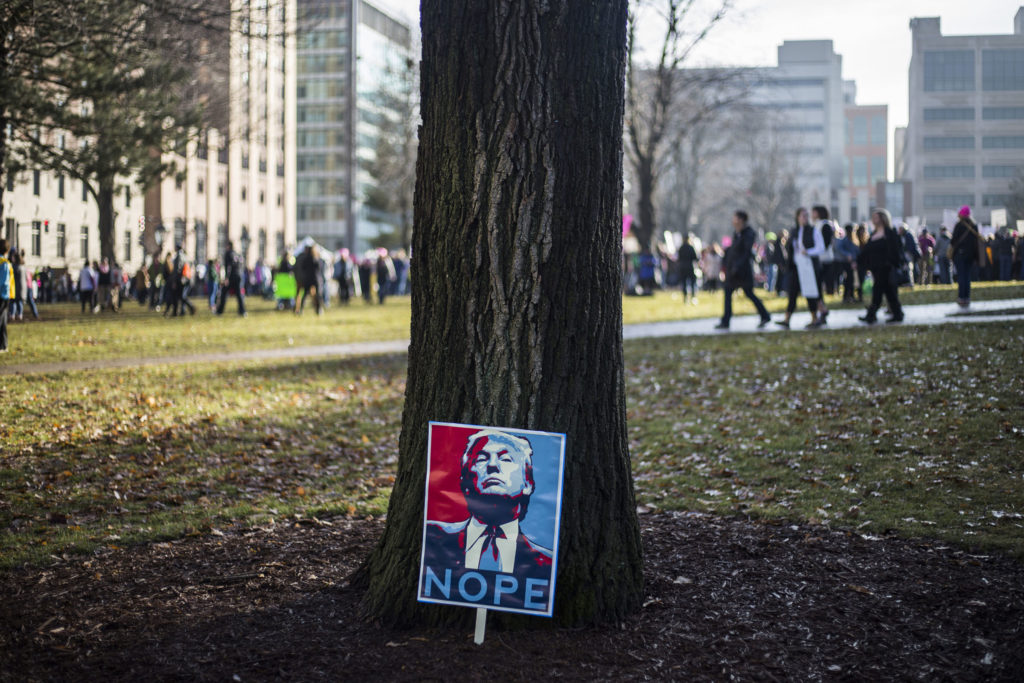 A sign leans against a tree outside of the Michigan State Capitol Building as attendees begin to return home from the Women's March in Lansing, Mich., on Saturday, January 21, 2017. (Photo by Brittany Greeson/GroundTruth)
