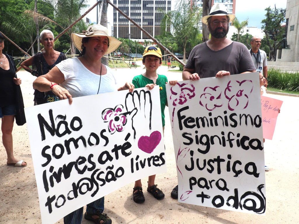 Demonstrators hold signs reading "We are not free until everyone is free" and "Feminism means justice for all." (Photo by Catherine Osborn/GroundTruth)