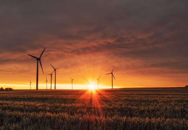 Wind turbines spin through sunset hours (Photo via Creative Commons).
