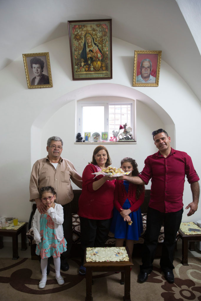 Anton Qulibyoba Yoakim (left) with his wife, son and granddaughters, as they hold a platter of Maamoul cookies, traditionally served in the Easter holiday. Their family was among the last remaining Christians in the biblical village of Emmaus, where Anton grew up. He now lives with his family in the old City of Jerusalem. (Photo by Heidi Levine/ GroundTruth)