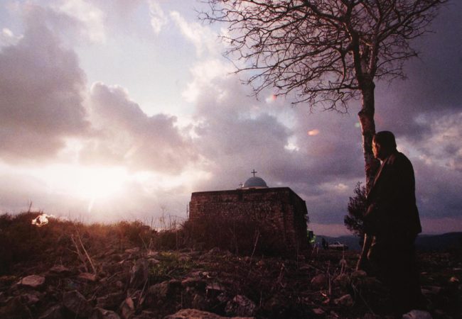 Elias Khoury, a Christian Arab, gazes at the church in Iqrit in December 1998. Khoury was born in Iqrit, where residents were forced out a half-century ago. On Christmas, they still attend services at the old stone church. (Photo by Heidi Levine)