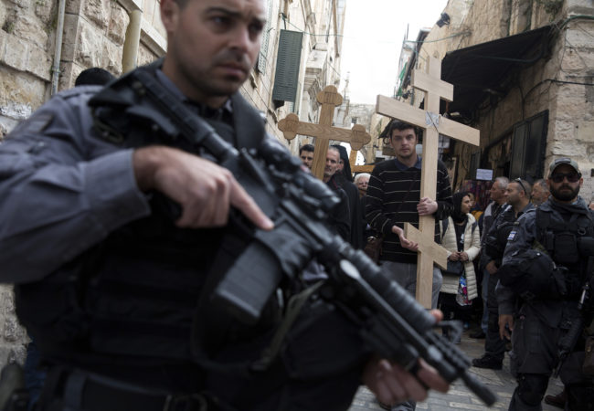 Israeli border police stand on guard as Christian pilgrims from Serbia carry wooden crosses along Via Dolorosa, or “The Way of Sorrow," in the Old City of Jerusalem on April 14, 2017. (Photo by Heidi Levine/GroundTruth)