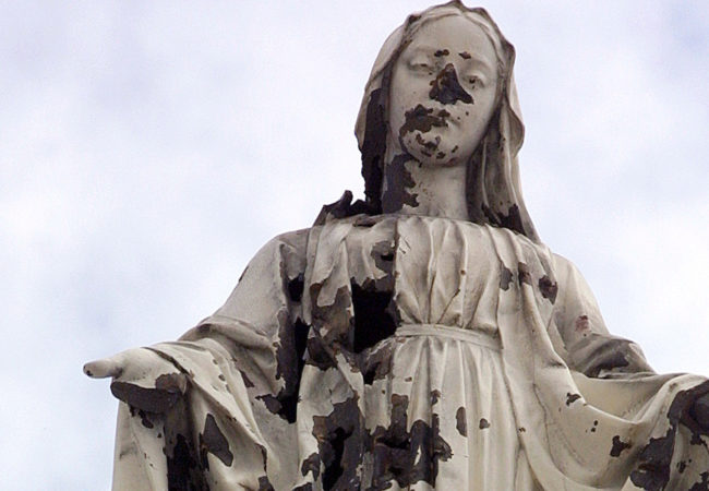A damaged statue of the Virgin Mary stands atop the chapel of the Holy Family Hospital and Orphanage in Bethlehem. The statue was hit by shrapnel when a shell from an Israeli tank slammed into the church during a predawn attack on March 14, 2002. (Photo by Heidi Levine)