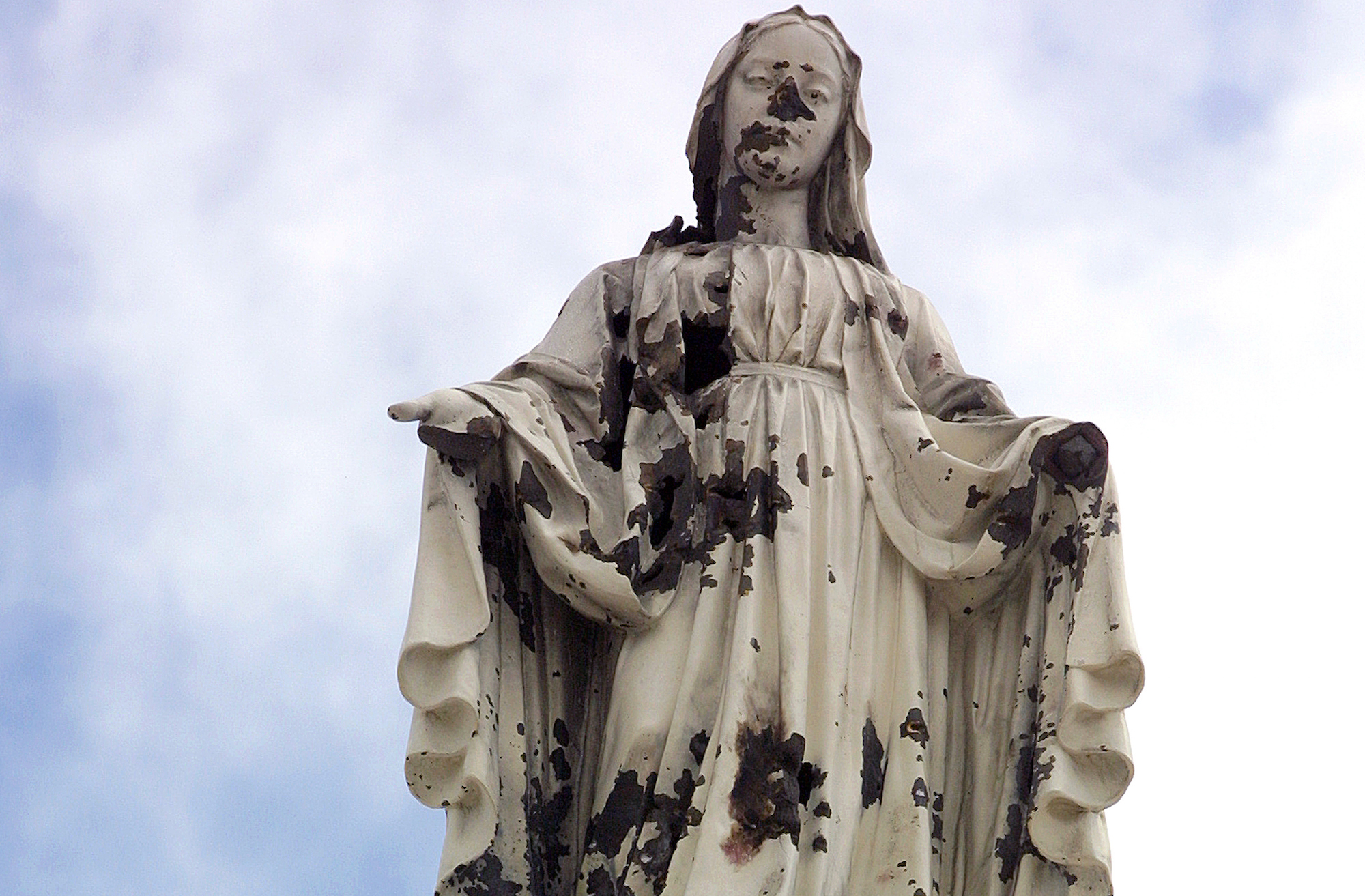 A damaged statue of the Virgin Mary stands atop the chapel of the Holy Family Hospital and Orphanage in Bethlehem. The statue was hit by shrapnel when a shell from an Israeli tank slammed into the church during a predawn attack on March 14, 2002. (Photo by Heidi Levine)