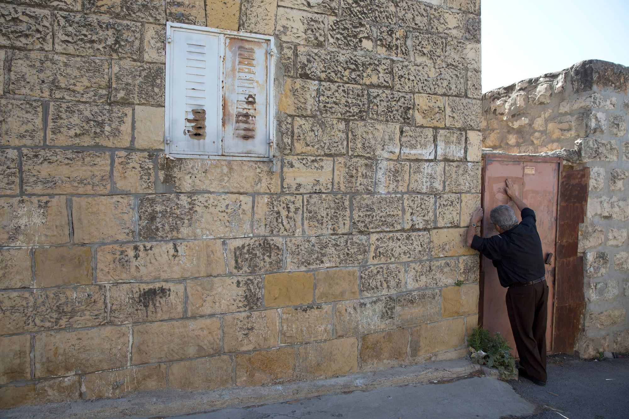 Anton Qulibyoba Yoakim, 63, bangs on the metal door of the home he grew up in the West Bank village of El Qubeibeh, on Monday, April 17, 2017. He now lives in the Old City of Jerusalem with his family. (Photo by Heidi Levine/GroundTruth)