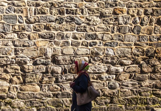 A woman walks alongside a brick wall (Photo via Pixabay)