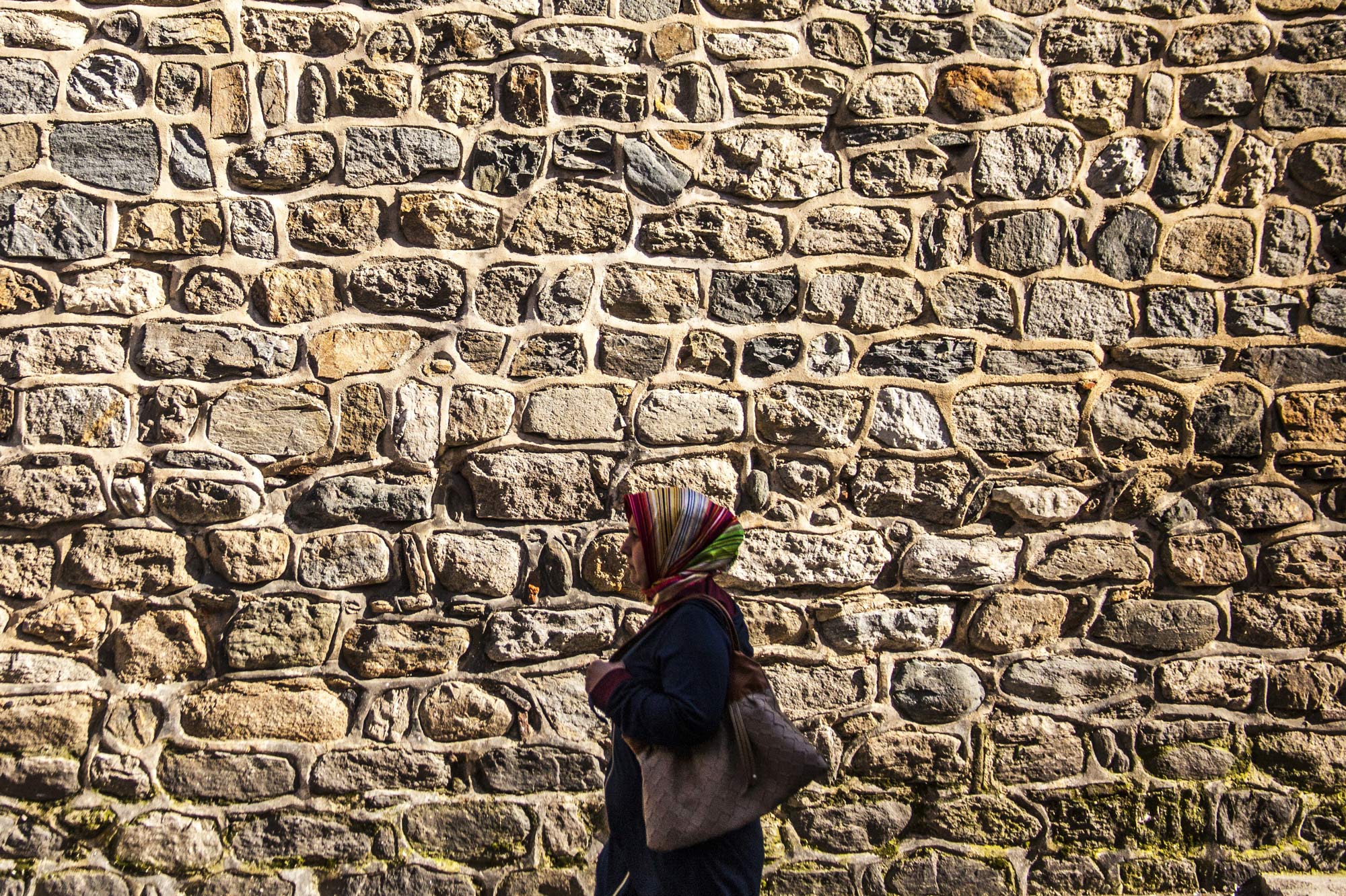 A woman walks alongside a brick wall (Photo via Pixabay)