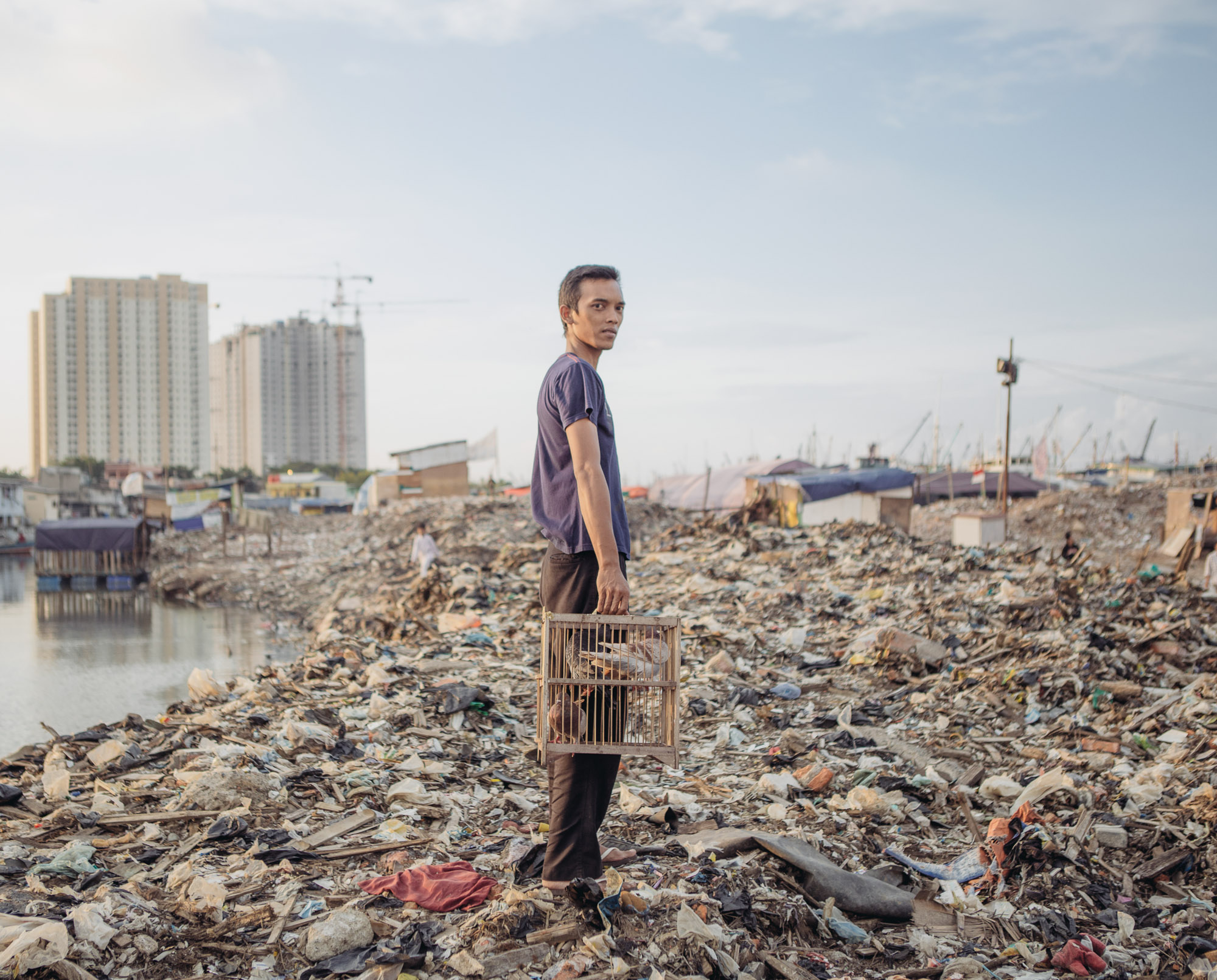 A man with his pigeons posed for photographs in Pasar Ikan district of North Jakarta. As part of Jakarta's river revitalization project, a settlement in this district was recently razed, leaving its residents homeless. It's part of an effort to combat sea level rise, worsened by climate change. (Photo by Muhammad Fadli/GroundTruth)