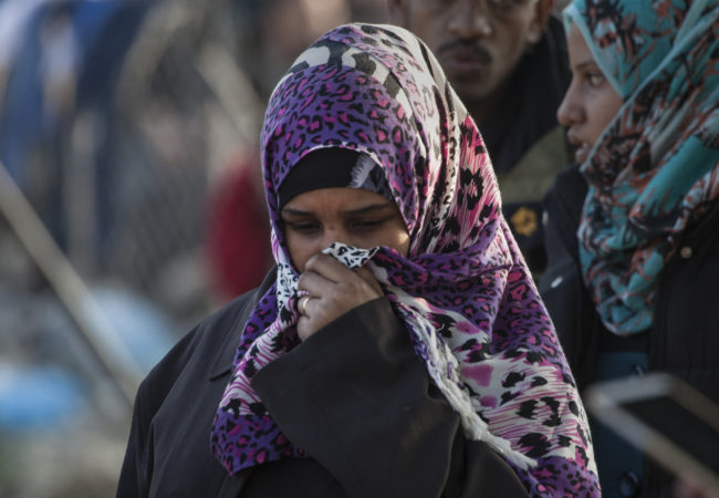 A woman stands and covers her face in Greece among a crowd of other refugees. (Photo by Steve Evans/Flickr Creative Commons)