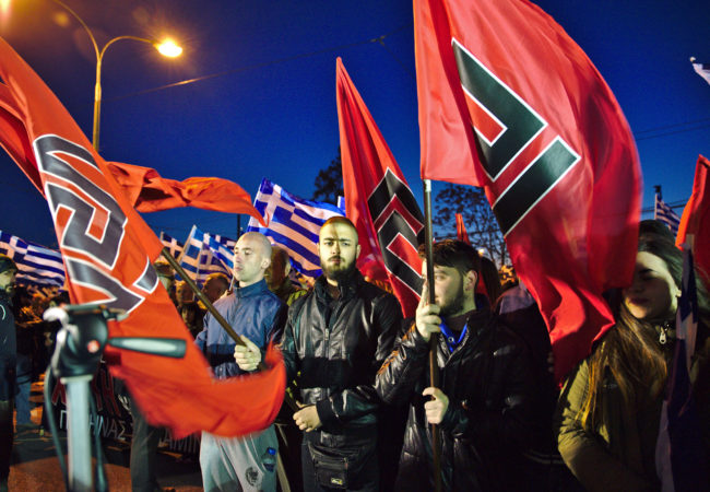 Golden Dawn members hold their party's flags during a March 2015 rally in Athens, Greece. (Photo via Wikimedia Commons)