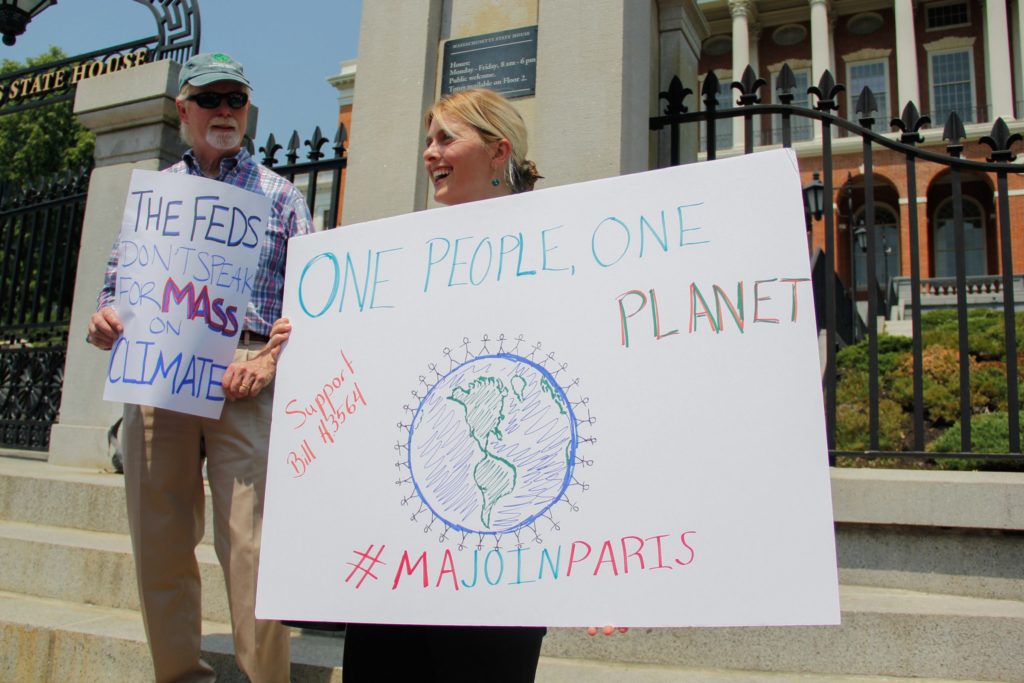 Rob Stenson, left, and Jessica Lambert show their support for the Paris Agreement outside the Massachusetts State House. Massachusetts has joined a coalition of states, known as the U.S. Climate Alliance, that have pledged to maintain the climate goals of the Paris Agreement. Additionally, the Massachusetts legislature is considering adopting a bill to make the climate goals a state law. (Photo by Ellen Kanzinger/GroundTruth)
