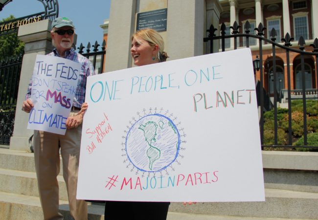 Rob Stenson, left, and Jessica Lambert show their support for the Paris Agreement outside the Massachusetts State House. Massachusetts has joined a coalition of states, known as the U.S. Climate Alliance, that have pledged to maintain the climate goals of the Paris Agreement. Additionally, the Massachusetts legislature is considering adopting a bill to make the climate goals a state law. (Photo by Ellen Kanzinger/GroundTruth)