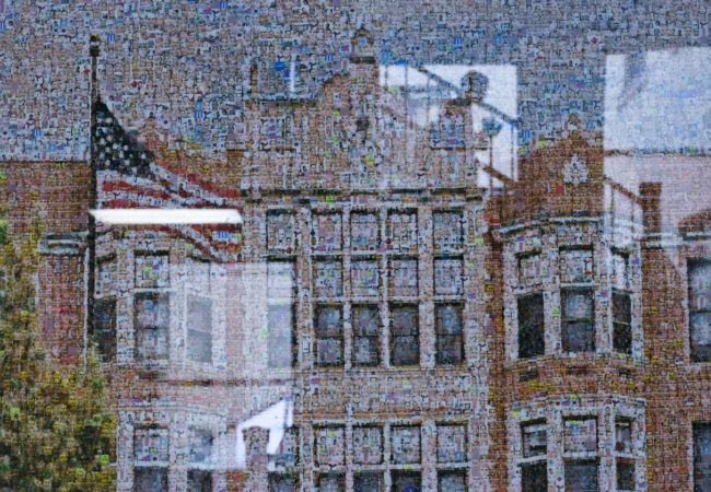 A student is reflected in a poster showing the student faces of the High School of Commerce within the building's likeness in Springfield, Mass., on Friday, September, 8, 2017. (Photo by Brittany Greeson)