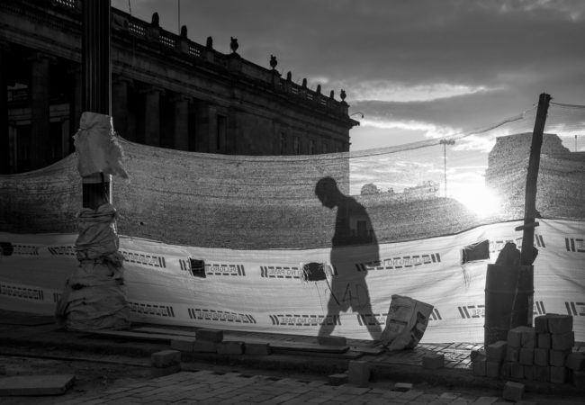 A man walks behind a construction barrier in the Plaza de Bolivar. In the background, the Colombian Congress Building. July 25, 2015. (Juan Cristóbal Cobo/The GroundTruth Project)