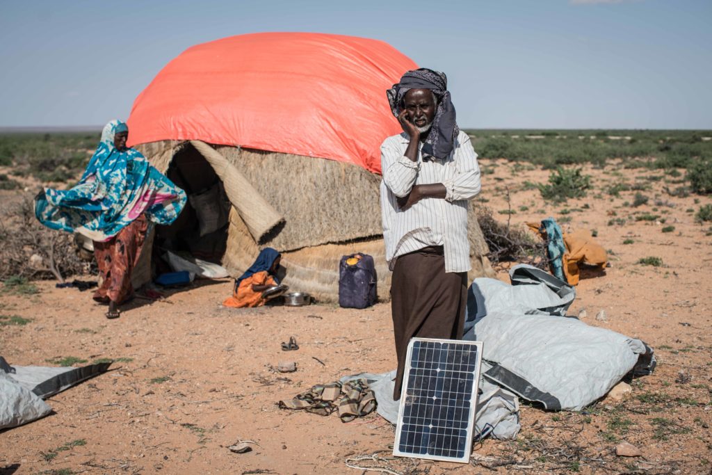 A man stands behind a solar panel in front of his home in Somalia as he talks on his cell phone. (Photo by Nichole Sobecki)