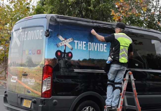 JC strips the "Crossing the Divide" wrap off the van. (Screenshot)