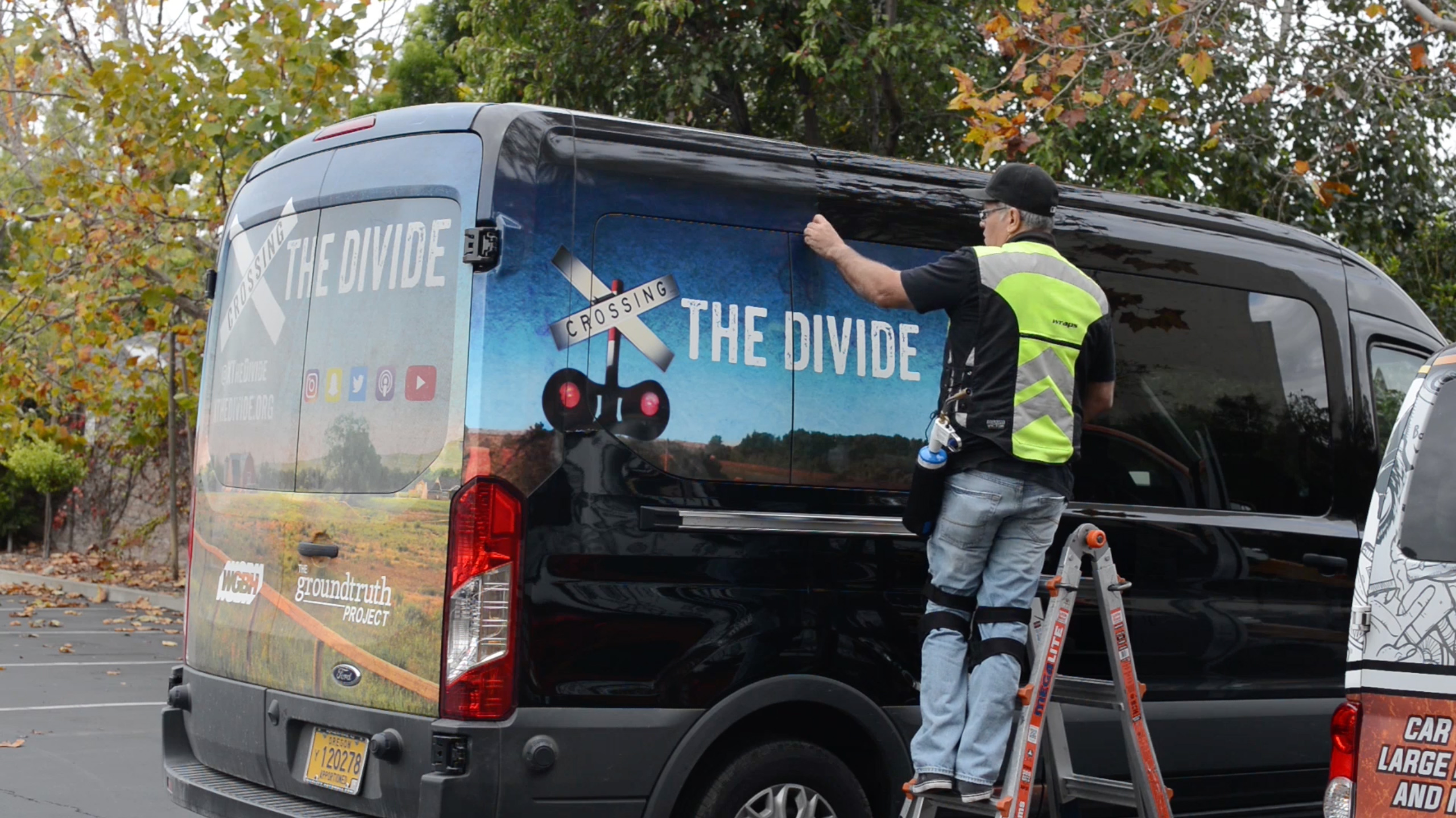 JC strips the "Crossing the Divide" wrap off the van. (Screenshot)