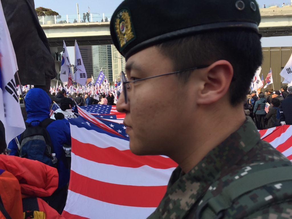 A South Korean soldier walks through a political march near Seoul Station featuring thousands of Korean and American flags on Saturday, March 10, 2018. (Kevin Grant/GroundTruth)