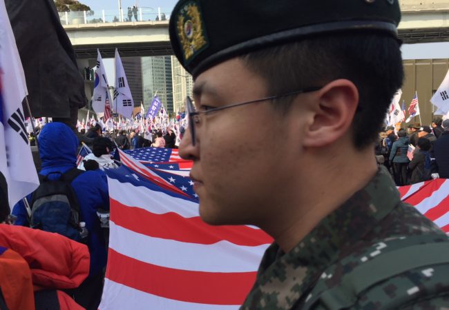 A South Korean soldier walks through a political march near Seoul Station featuring thousands of Korean and American flags on Saturday, March 10, 2018. (Kevin Grant/GroundTruth)