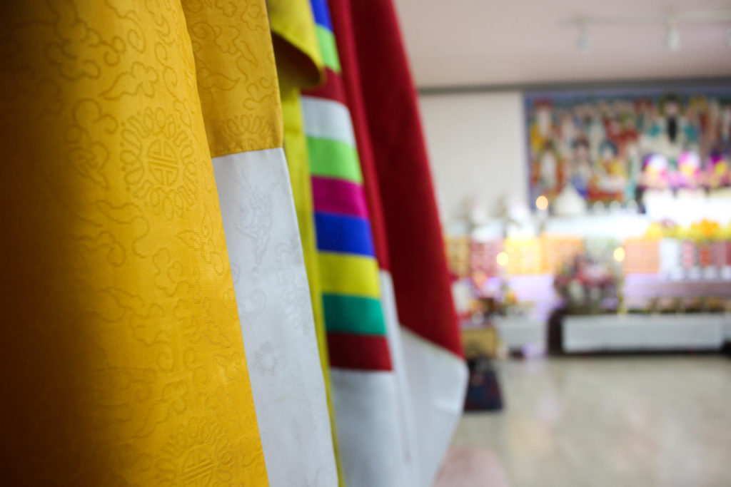 A collection of silk robes lines one of the walls. The five-hour ceremony is divided in shorter segments of about 30 minutes each. During each segment, the four shamans are believed to incarnate one of the many gods in Korean shamanism. Every time they did so, they changed the color of their robe. (Miranda Mazariegos/GroundTruth)