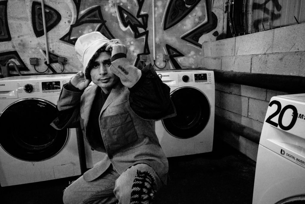 Faiz Mohammad Bashardot, an Afghan man staying at La Bulle, poses next to a washing machine inside La Bulle's accommodation center. (Photo by Annabelle Marcovici/GroundTruth)