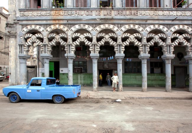 A man stands on the street next to a vintage car in Cuba. (Photo by Falkenpost/Pixabay)
