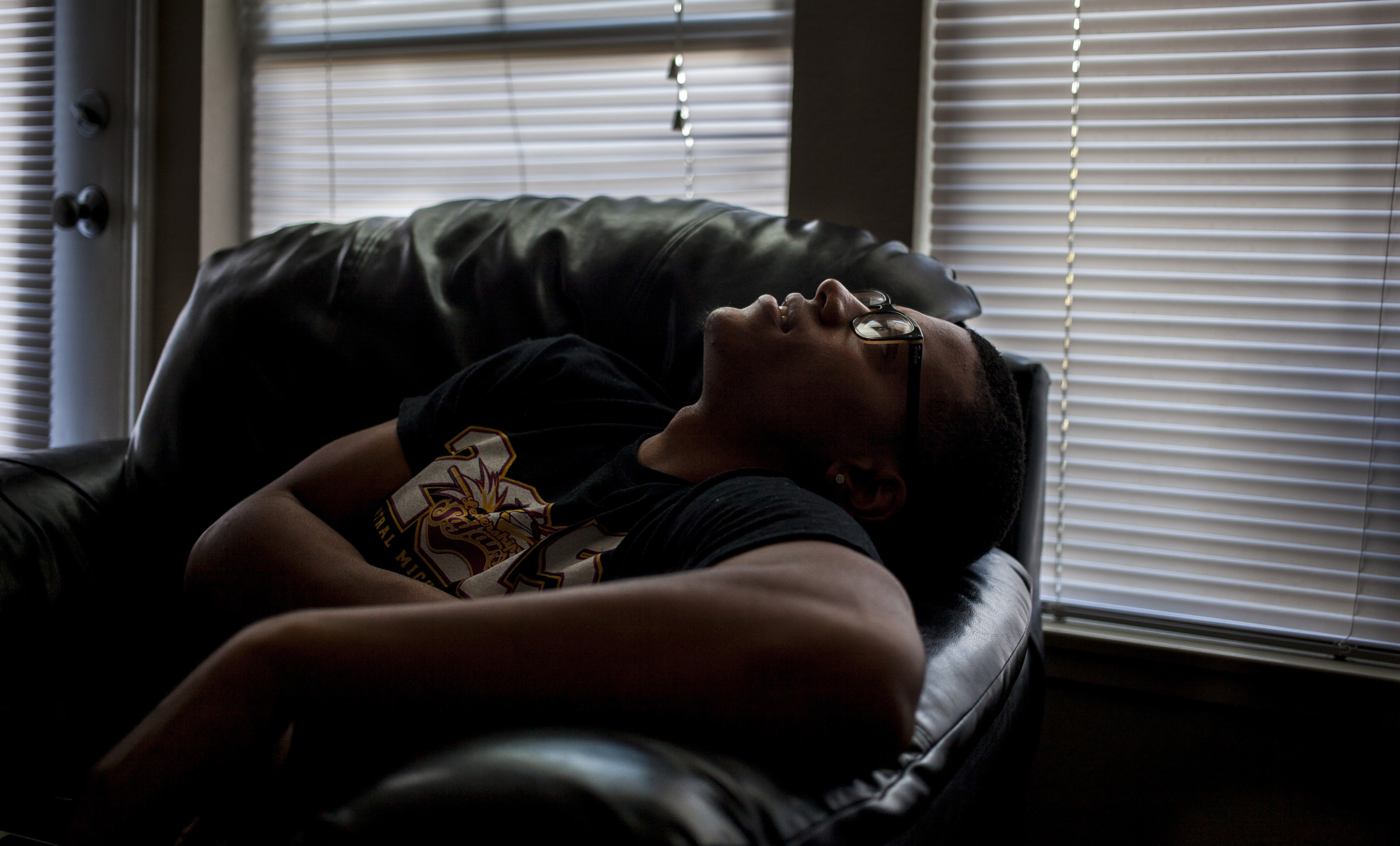 Trenton Carson relaxes in his apartment as light filters in through the blinds. Carson doesn't let micro aggressions bother him because he says, “People who aren’t black don’t see what we go through… because people don’t want to." He goes on to say. “We’re all uncomfortable in this world… only thing that’s different it where we come from.” (Photo: Josephine Norris/GroundTruth)
