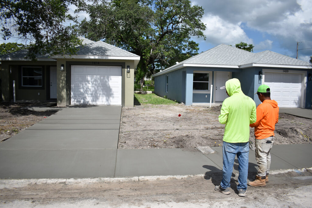 Two construction workers stand over freshly poured cement in front of newly built affordable homes in Florida.