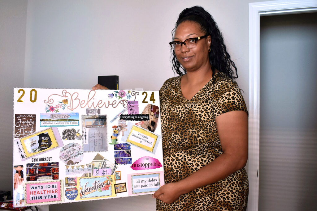 A woman with brown skin, glasses and a long black ponytail holds up her 2024 vision board.