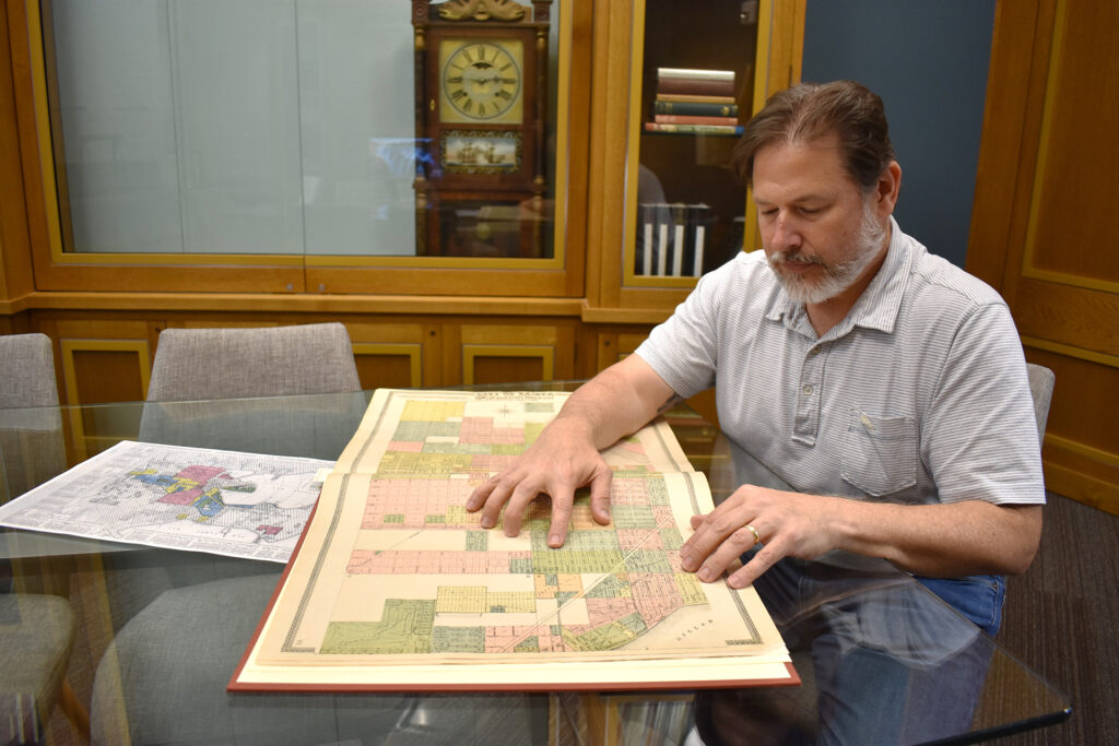 A man with pale skin, brown hair and a beard uses a map to show where areas were redlined in Tampa, Florida.
