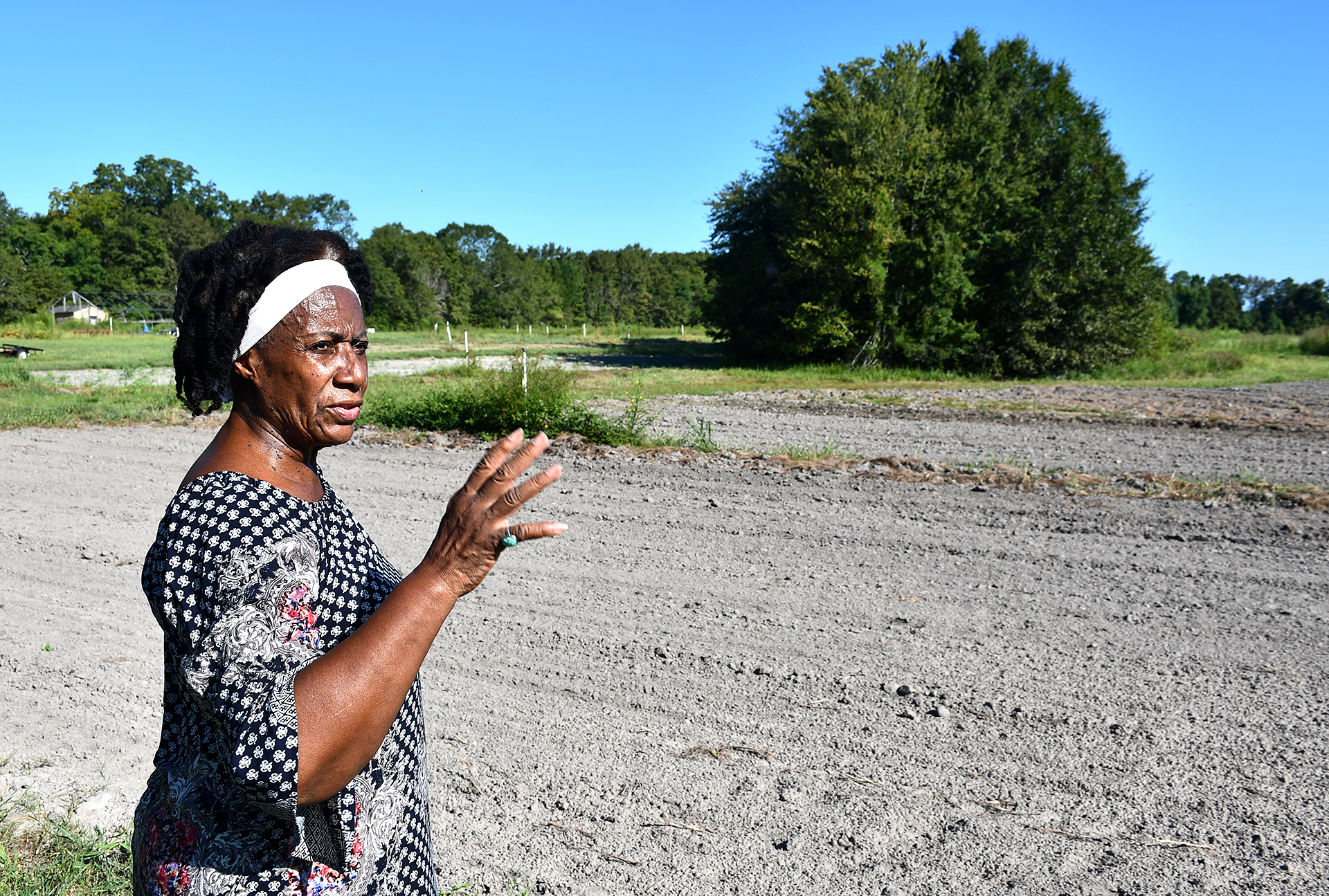 A woman middle-aged with brown skin and black hair talks about her farm while standing in front of a plot of land.