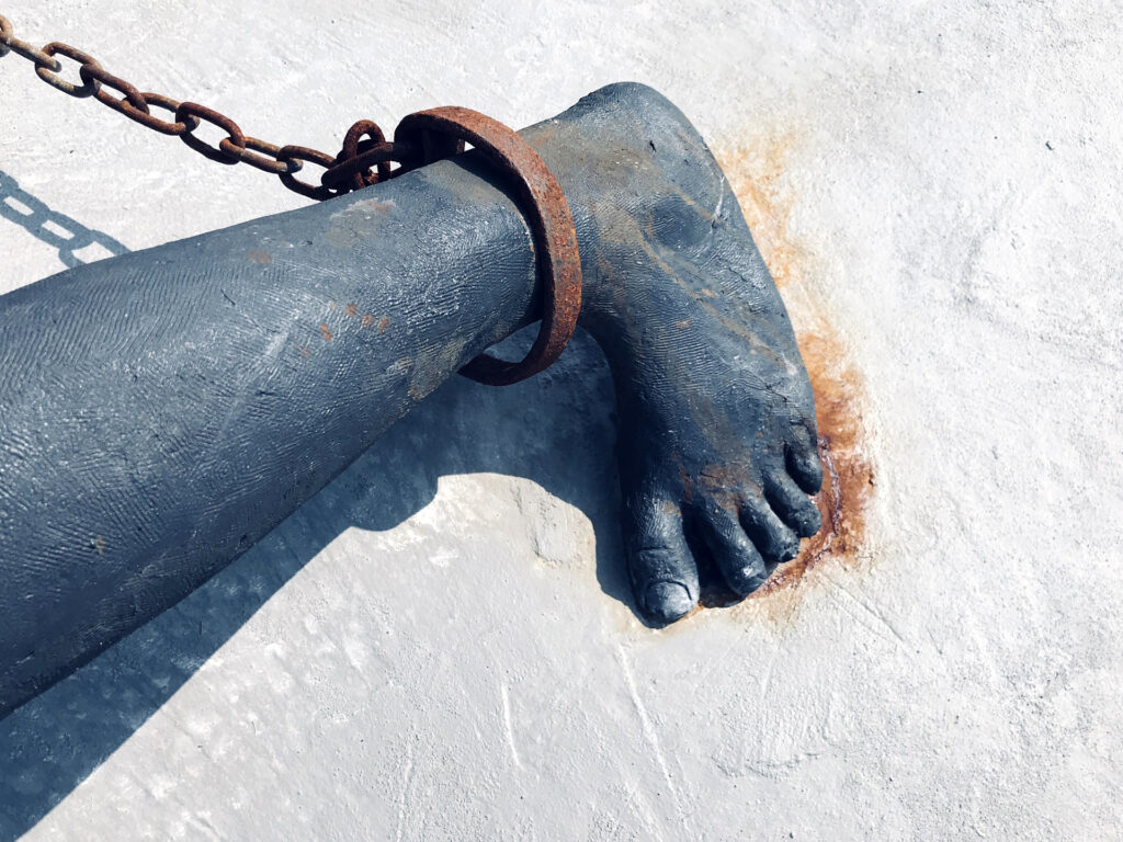 This image features a black sculpture of a foot with a chain around it.