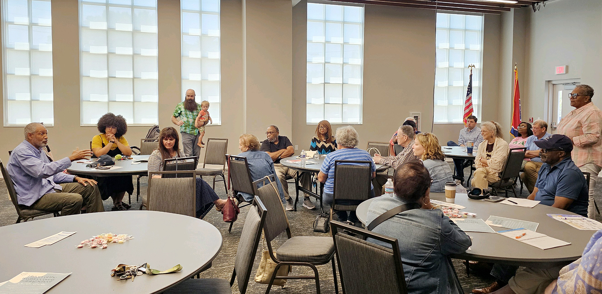 A group of people have a discussion while sitting around tables in a conference room.