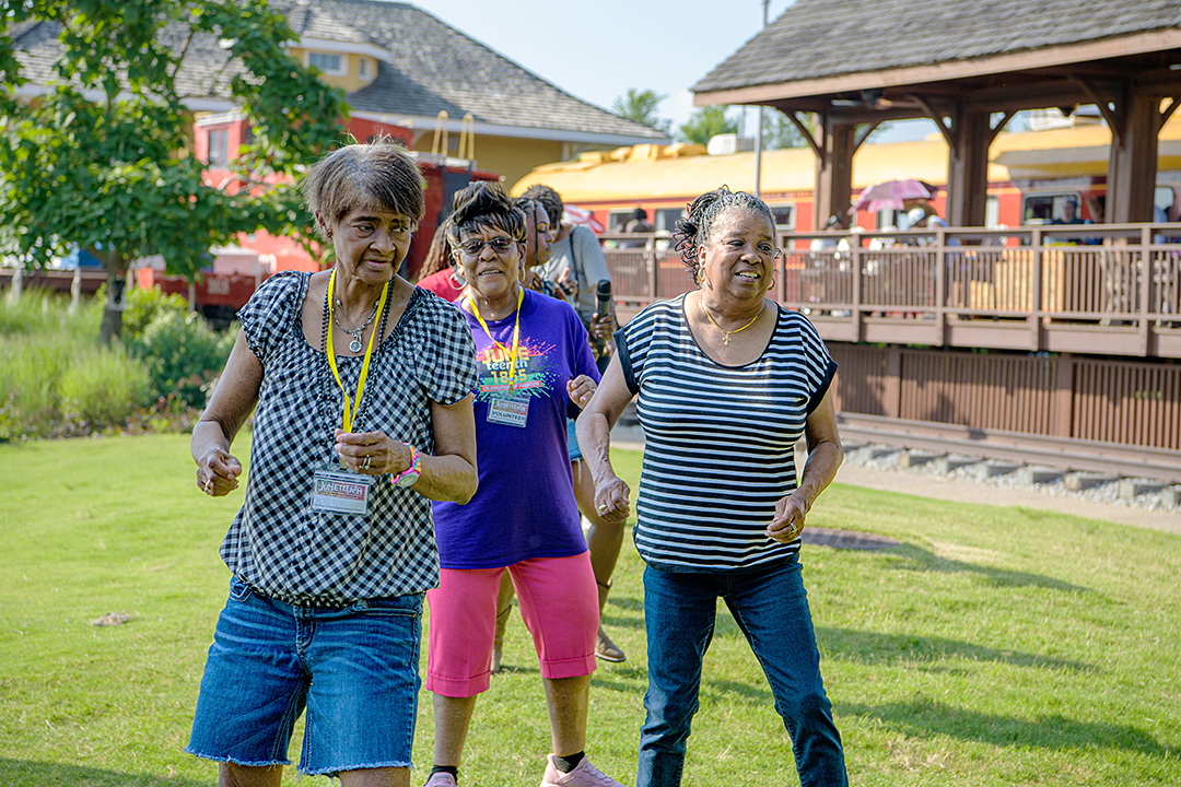 Three middle-aged women with brown skin do a line dance at a festival